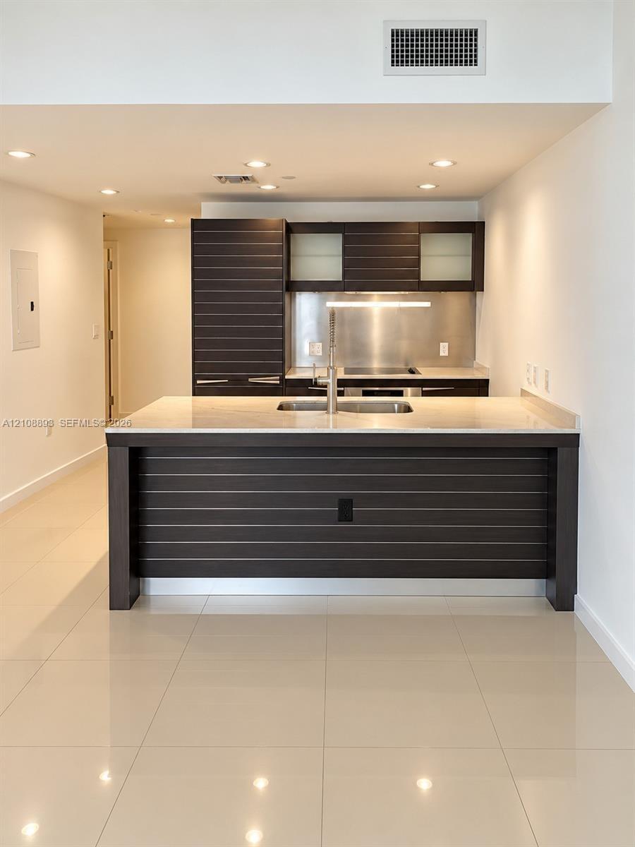 Kitchen featuring dark wood-finish cabinetry with horizontal slat detailing, stone-surface island countertop, integrated stainless steel backsplash, a