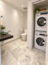 Full-bathroom featuring large-format stone-patterned floor tile, glass vessel sink with dark floating vanity, integrated laundry closet, and decorativ