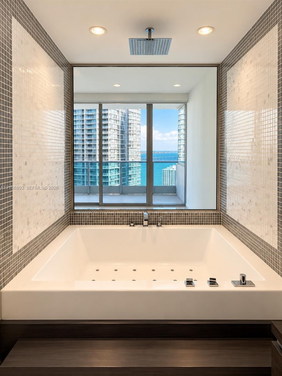 Drop-in soaking tub with a deck-mounted faucet, square rain shower head, large-format mirror, and custom mosaic tile surround
