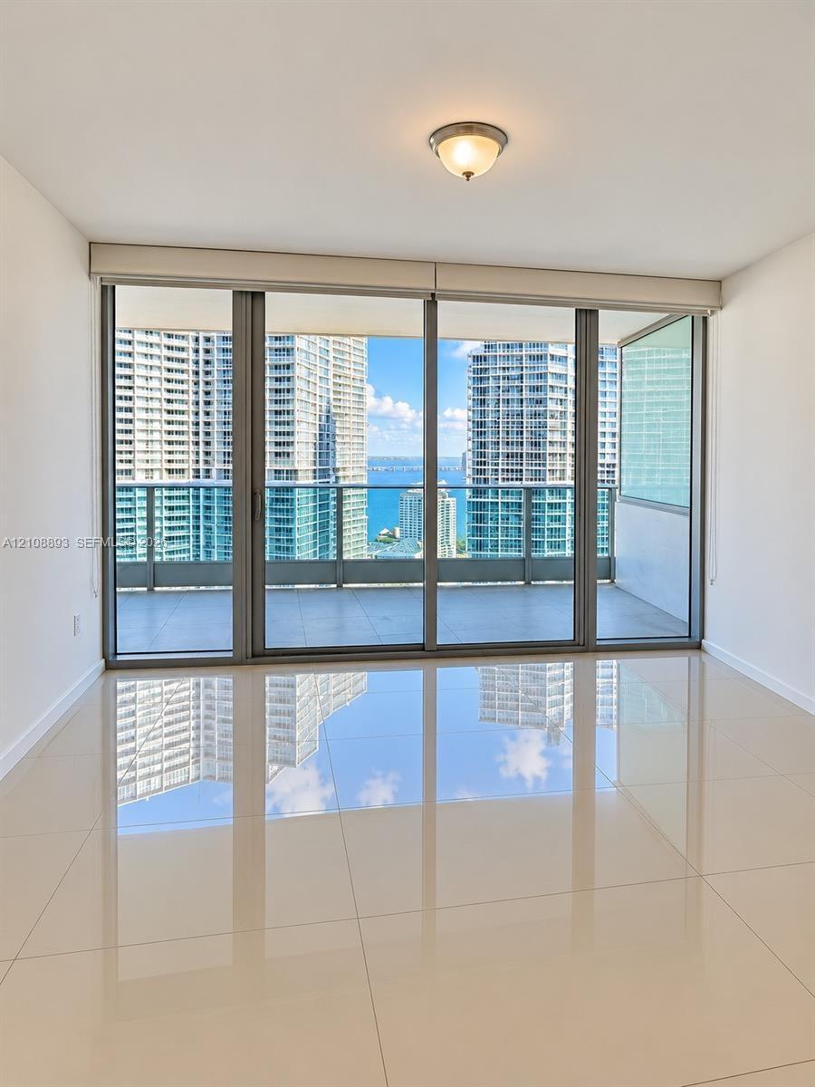 Floor-to-ceiling sliding glass doors, expansive covered balcony, polished tile flooring, and flush-mount lighting