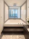 Built-in soaking tub with a raised dark wood-finish platform, overhead rainfall showerhead, mosaic tile surround, and expansive window showcasing wate