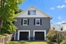 Two-story exterior featuring a textured masonry facade, wood-shingle gables, double-car garage with black paneled doors, and a natural stone retaining