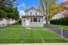 Two-story home with grey vinyl siding, white trim, a multi-pane front entry door, a paved driveway, and a chain-link fenced front yard *virtually edit