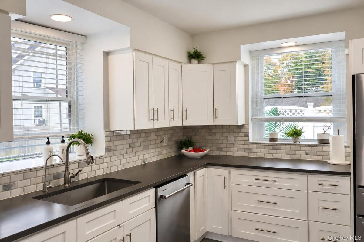Kitchen featuring shaker-style cabinetry, dark solid-surface countertops, subway tile backsplash, stainless steel appliances, and dual windows