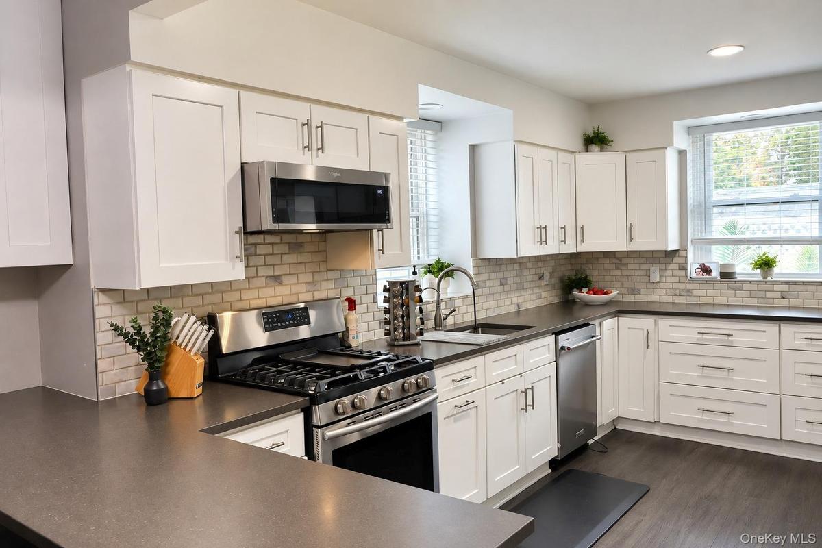 Kitchen featuring white shaker-style cabinetry, stainless steel appliances, dark composite countertops, and a light-toned brick-style tile backsplash