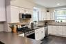 Kitchen featuring white shaker-style cabinetry, stainless steel appliances, dark composite countertops, and a light-toned brick-style tile backsplash