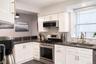 Kitchen featuring white shaker-style cabinetry, dark stone countertops, subway tile backsplash, stainless steel gas range with overhead microwave, and