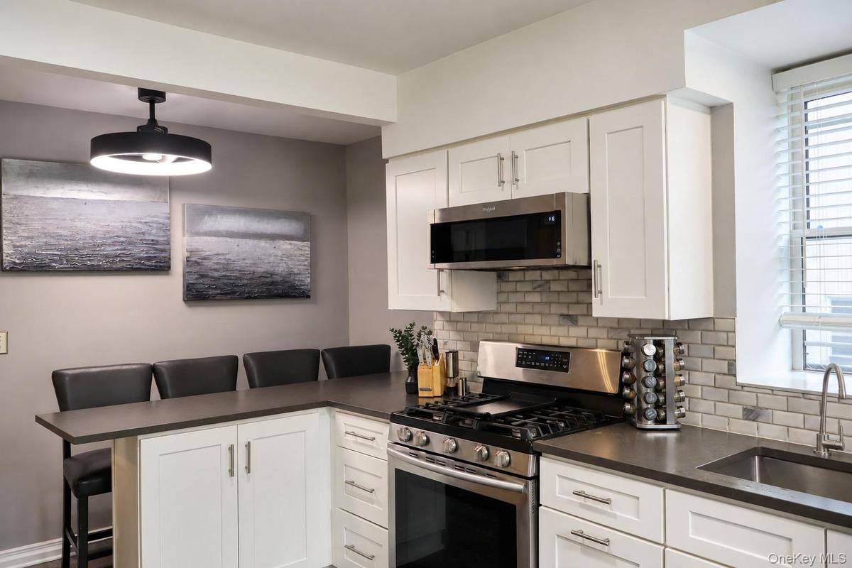 Kitchen featuring white Shaker-style cabinetry, dark solid-surface countertops, stainless steel appliances, subway tile backsplash, and a contemporary