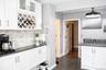 Kitchen featuring white cabinetry with integrated wine rack, stone-tiled backsplash, dark solid-surface countertops, wood-finish flooring, and a moder