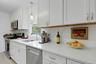 Kitchen with appliances with stainless steel finishes, pendant lighting, light stone counters, white cabinets