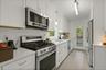 Kitchen with appliances with stainless steel finishes, pendant lighting, light stone counters, white cabinets, and light wood-style floor