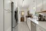 Kitchen with appliances with stainless steel finishes, pendant lighting, light stone counters, white cabinets