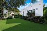 Stucco exterior featuring dual glass-paneled doors, wrought-iron railing, manicured lawn, and lush landscaping
