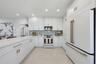 Kitchen featuring white shaker-style cabinetry, quartz countertops, a green and white vertical tile backsplash, gold-toned hardware, and white-finish 