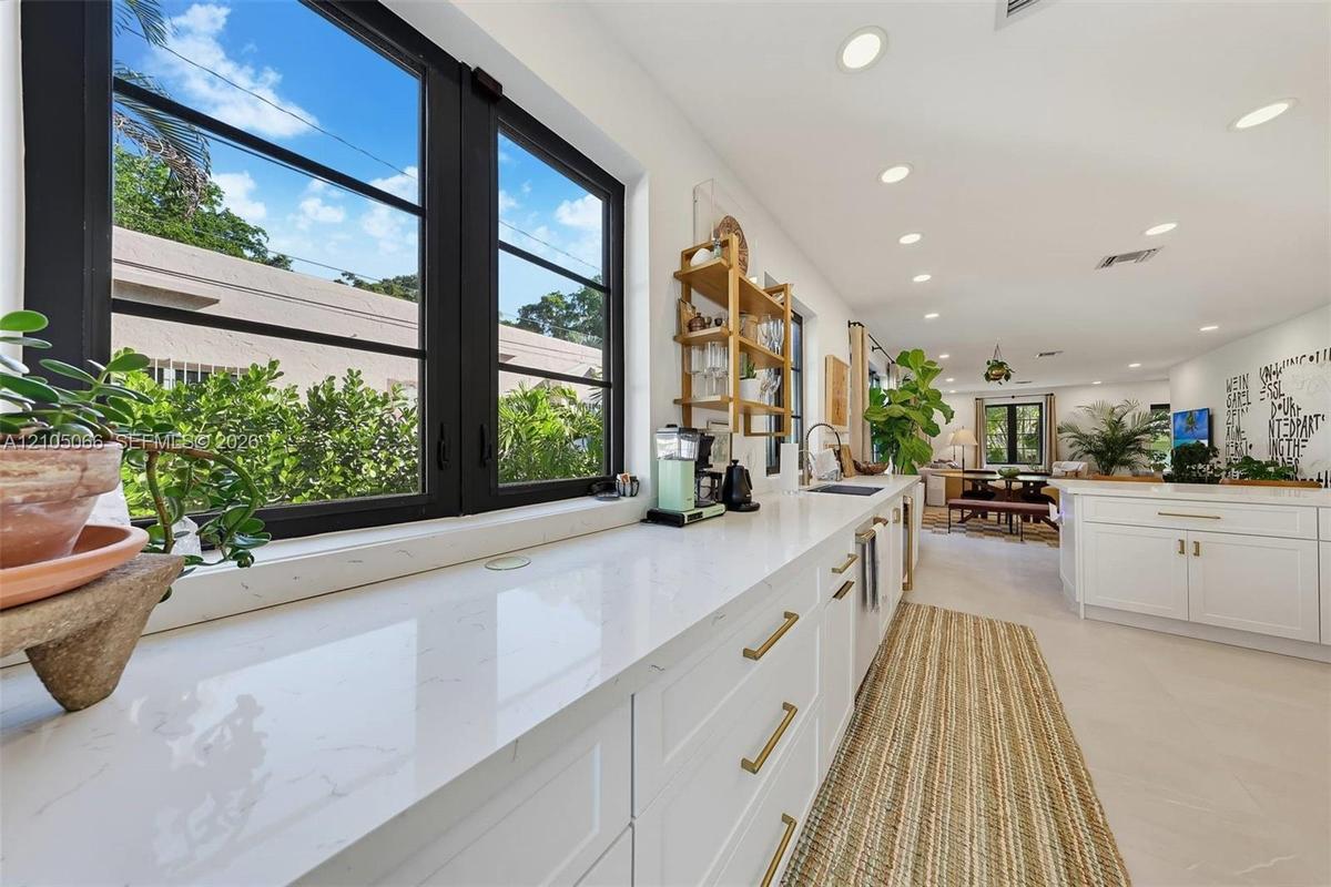 Kitchen featuring white cabinetry with gold-toned hardware, solid-surface countertops, recessed lighting, and black-framed windows