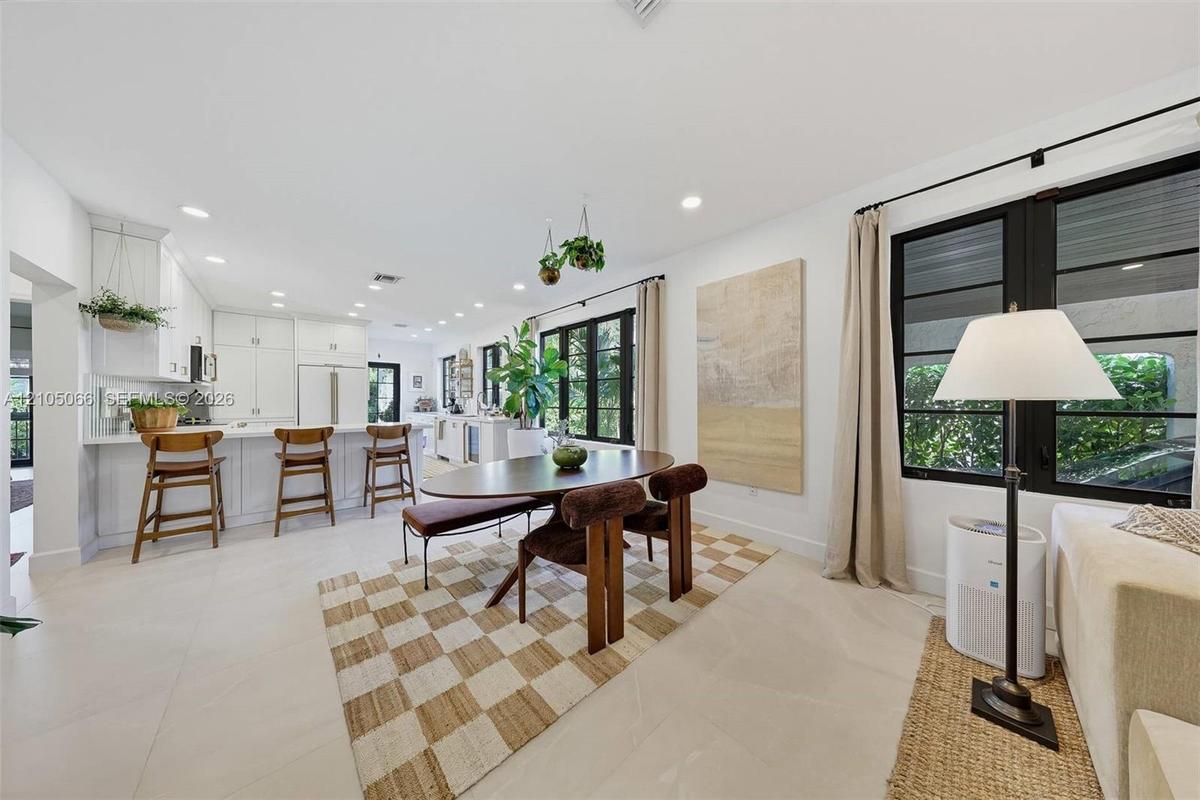 Open-concept kitchen and dining area featuring white shaker-style cabinetry, a central island with bar seating, large-format tile flooring, and oversi