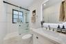 Bathroom featuring a vanity with a white countertop and brass-finish widespread faucet, a backlit mirror, a tub-shower combination with a sliding glas