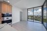 Floor-to-ceiling glass sliding doors, light-toned tile flooring, built-in wall oven and microwave, custom wood-finish cabinetry, and stone-surface cou
