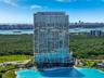 High-rise residential tower featuring a glass-curtain wall exterior, private balconies, and a multi-level structure positioned on a waterfront site wi