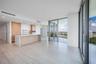 Open-concept kitchen featuring wood-finish cabinetry, a waterfall-edge stone island, built-in stainless steel appliances, wood-finish flooring, and fl