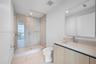 Bathroom featuring wood-finish cabinetry, a large integrated mirror, a walk-in shower with a glass enclosure and floor-to-ceiling wall tile, and light