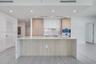 Kitchen featuring a center island with a stone-finish waterfall countertop, custom wood-finish cabinetry, white matte upper cabinets, integrated stain