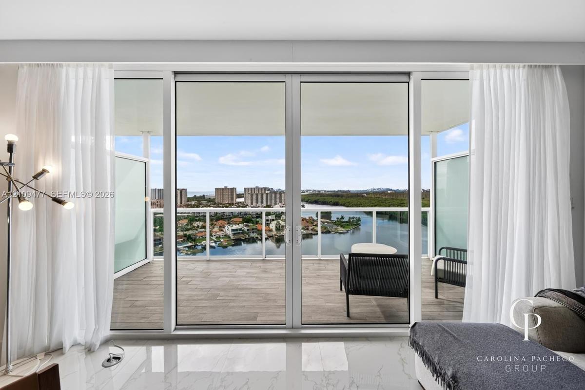 Floor-to-ceiling glass sliding doors opening to a covered balcony with tiled flooring and a glass panel railing