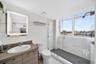 Bathroom featuring a wood-finish vanity with an integrated basin, a backlit mirror, and a walk-in shower with stone-tile surround, dark floor tiling, 