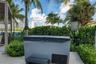 Outdoor hot tub featuring a hard-top cover and integrated step, set on a paved patio with a modern pergola and lush perimeter landscaping