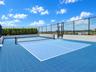 Rooftop athletic court with blue modular surface, perimeter chain-link fencing, and integrated privacy hedging