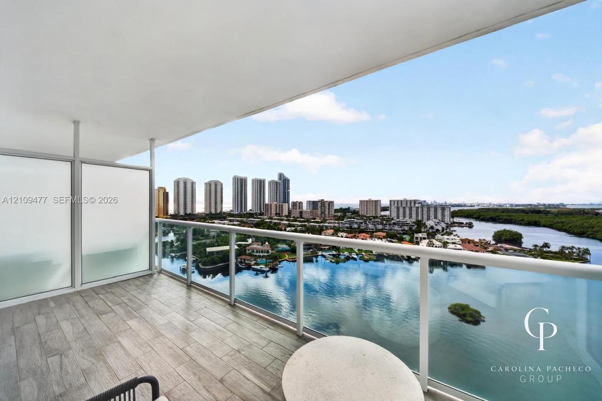 Covered balcony featuring wood-finish tile flooring, glass panel railing, and frosted privacy screens