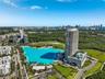 Aerial perspective of a high-rise residential tower featuring a multi-level podium, an attached swimming pool, landscaped grounds, and a central lagoo