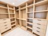 Custom walk-in storage featuring light wood-finish cabinetry, extensive built-in shelving, integrated garment rods, and two sets of drawers with matte