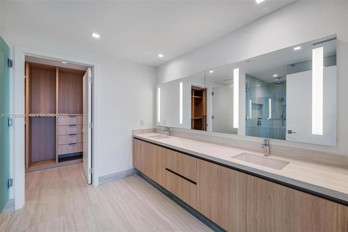 Floating double vanity with wood-finish cabinetry, integrated rectangular sinks, expansive wall-to-wall mirror with built-in vertical lighting, and la