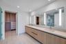Floating double vanity with wood-finish cabinetry, integrated rectangular sinks, expansive wall-to-wall mirror with built-in vertical lighting, and la