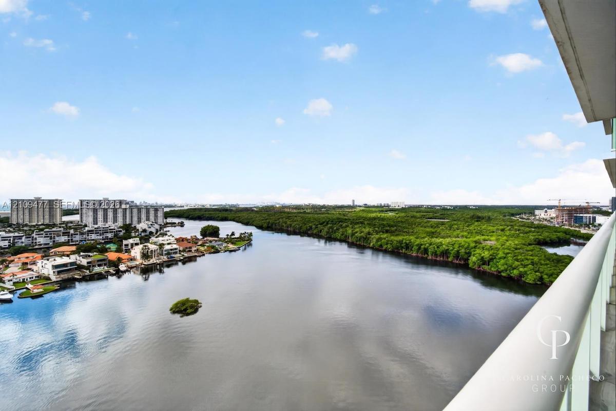 Elevated balcony featuring a glass-panel railing, expansive water frontage, and surrounding natural foliage