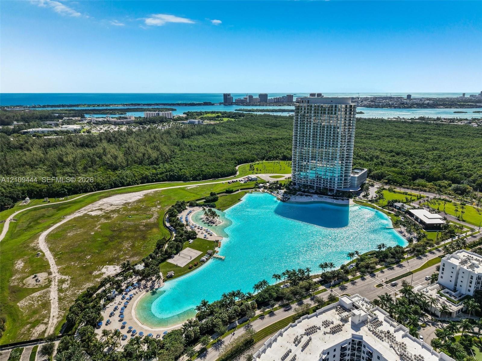 Aerial perspective featuring a high-rise residential tower and an expansive man-made crystalline lagoon with sandy shorelines