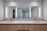 Dual-vanity cabinet with wood-finish cabinetry, neutral stone-composite countertop, integrated dual undermount sinks, and full-width mirror featuring 