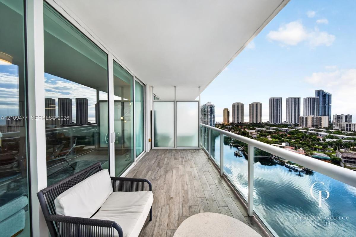 Covered balcony featuring wood-finish flooring, glass panel railings, frosted privacy screens, and floor-to-ceiling sliding glass doors