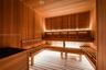Sauna featuring wood-plank wall paneling, multi-level slatted wood benches, hidden LED accent lighting, and a built-in heating unit
