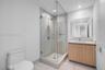 Walk-in glass shower with floor-to-ceiling tile, light wood-finish cabinetry, rectangular vessel sink, surface-mounted vanity mirror, and recessed lig