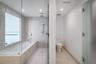 Bathroom featuring floor-to-ceiling stone-finish tile, glass-enclosed soaking tub with rain-style shower head, recessed lighting, and a private water 