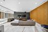 Large-format polished stone flooring, custom wood-paneled accent wall, dark stone-clad feature wall, floating built-in cabinetry, and full-height glas