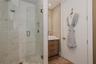 Walk-in shower featuring glass paneling, marble-style tile walls, and a pebble-stone floor, paired with a wood-finish vanity, vessel sink, and solid-c