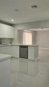Kitchen featuring white flat-panel cabinetry, stone-style countertops, integrated stainless steel dishwasher, and polished light-toned flooring