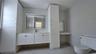 Bathroom featuring white cabinetry with integrated floor-to-ceiling storage, stone-surface countertop, rectangular wall mirror with integrated lightin