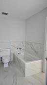 Bathroom featuring a deep soaking tub with a wall-mounted faucet, complemented by large-format tile flooring and matching tile surround