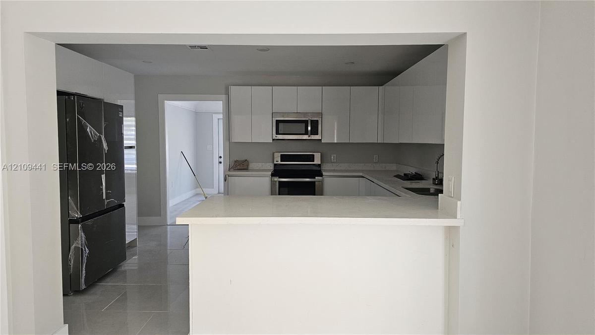 Kitchen featuring high-gloss white cabinetry, stainless steel appliances, a peninsula counter, and light-toned tile flooring