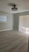 Neutral wall tones, wood-finish flooring, ceiling-mounted light fixture, sliding glass door with vertical blinds, and window with horizontal blinds