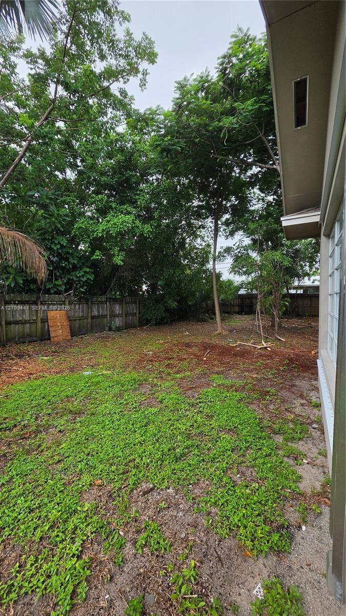 Rear yard featuring a wood fence, mature trees, and ground cover
